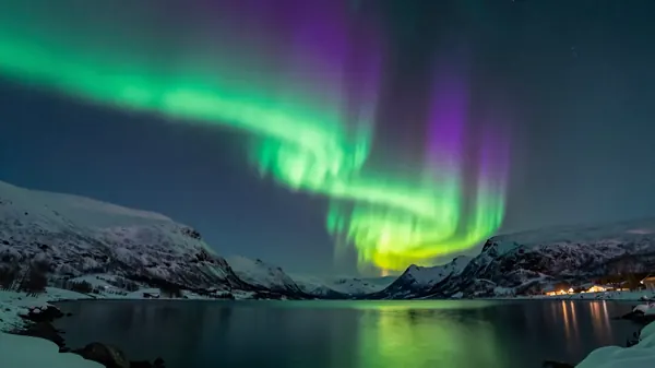 Green and purple northern lights over a snowy mountain lake at night