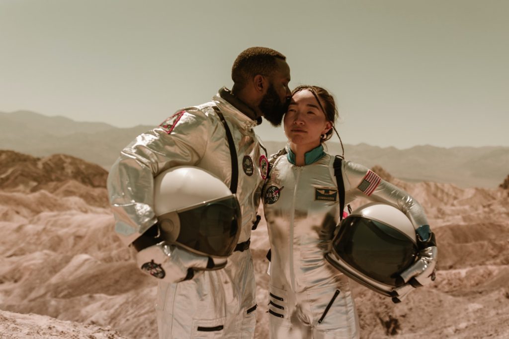 A Couple Wearing Space Suit While Holding Helmets